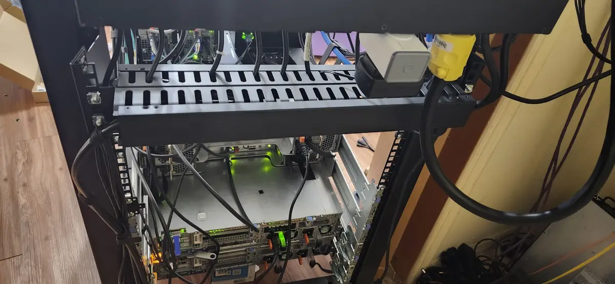 A close-up photo of a server rack with multiple servers and tangled cables, showing green power indicator lights. The…