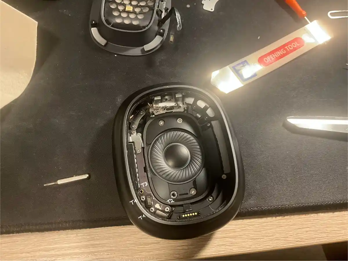 A disassembled black electronic device, likely a headphone or earbud, is shown on a workbench with its internal components…