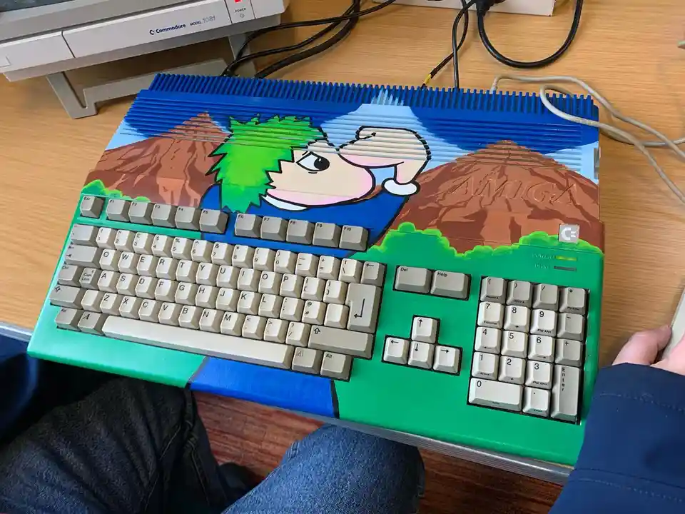 A close-up photo of a Commodore Amiga computer with a custom painted case featuring a cartoon character with green hair and…