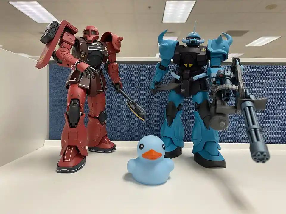 Two large, detailed robot action figures—one red and one blue—are standing on a white office desk, facing each other with…