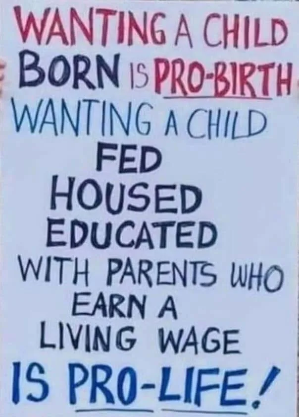 A handwritten sign with red and blue marker text on white paper. The top line reads 'WANTING A CHILD BORN IS PRO-BIRTH' with…
