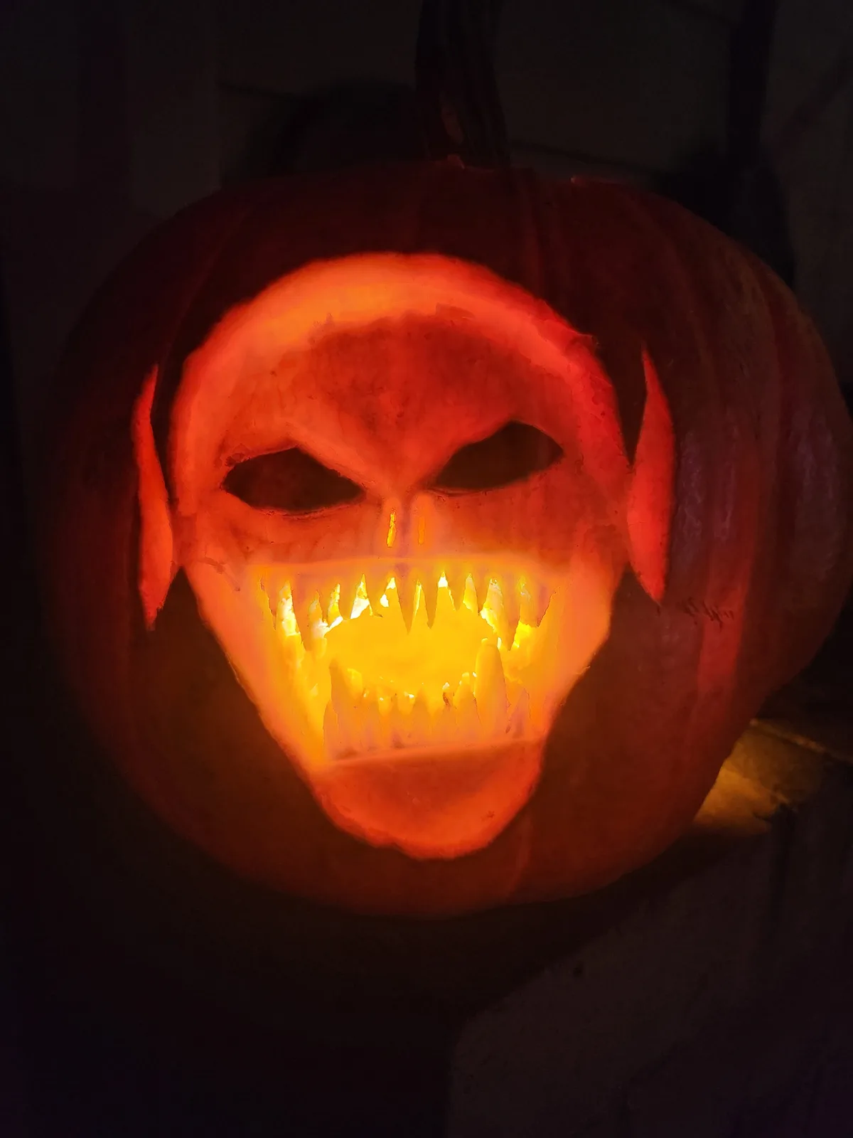 A close-up of a carved Halloween pumpkin illuminated from within, featuring a menacing face with sharp teeth, angular eyes…