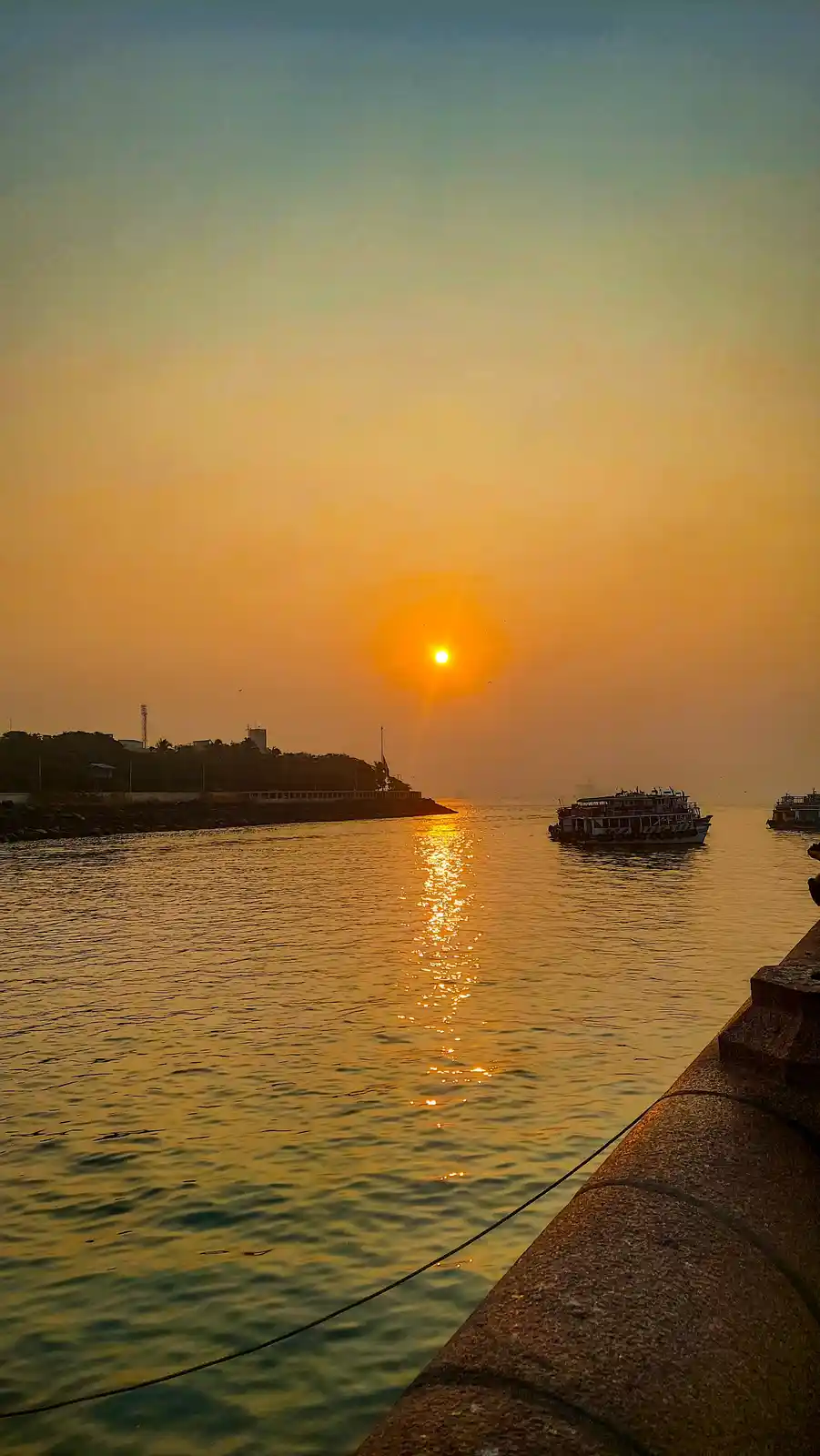 A serene sunrise over a body of water with a hazy orange sky, the sun low on the horizon casting a golden reflection on the…
