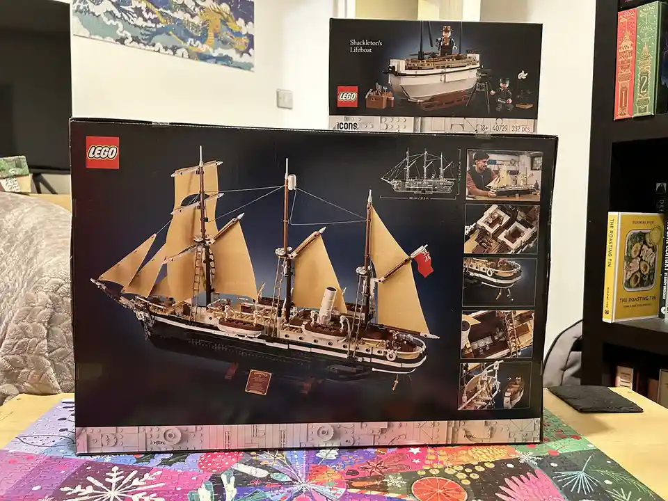 A large LEGO box for the 'Endurance' ship model sits on a table, with a smaller 'Shackleton's Lifeboat' box visible behind…