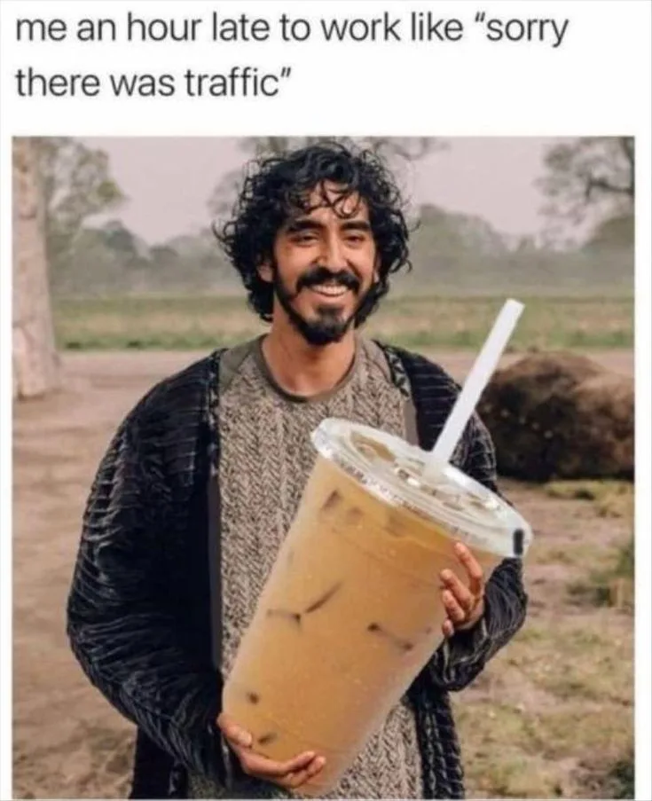 A man with dark curly hair and a beard, wearing a textured sweater and dark jacket, holds a giant plastic cup of iced coffee…