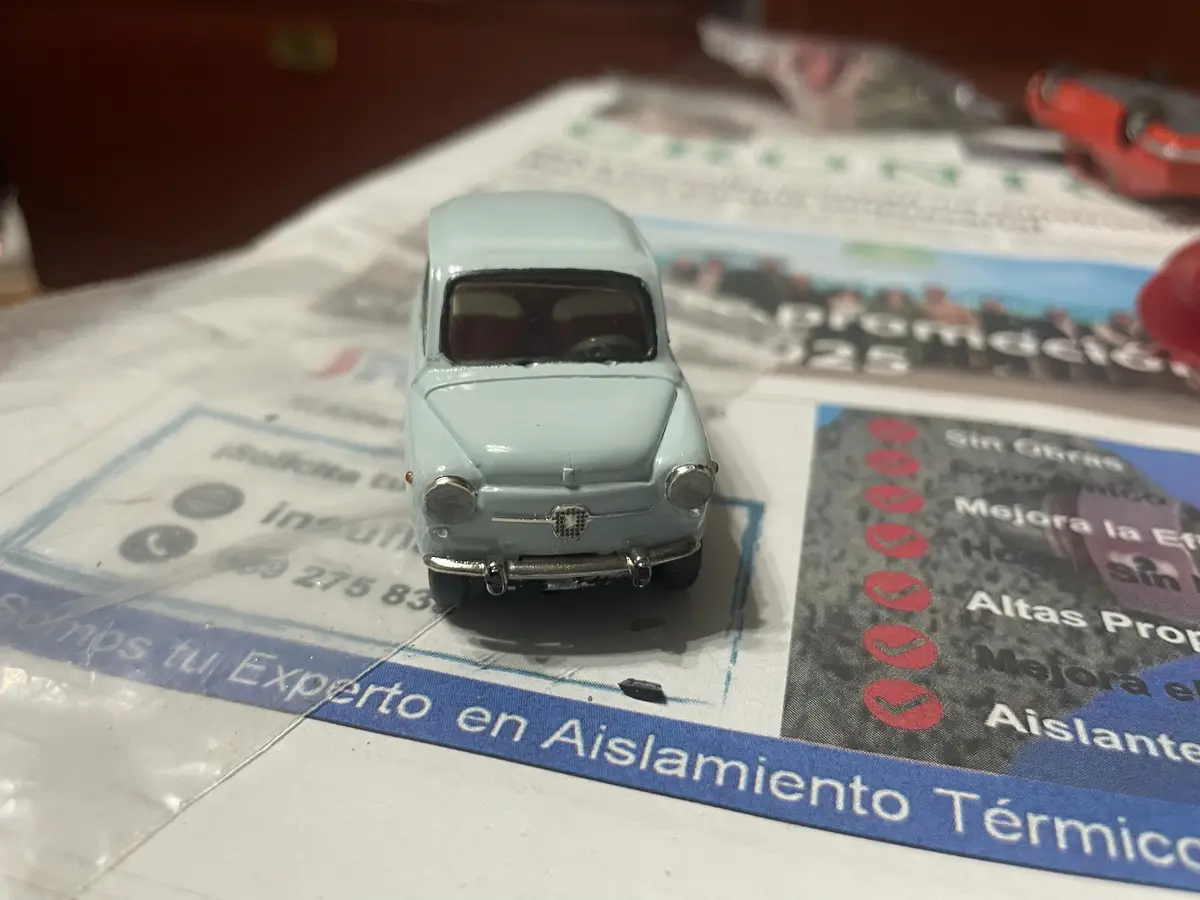 A small, light blue vintage toy car is positioned on a printed advertisement for thermal insulation services, which features…