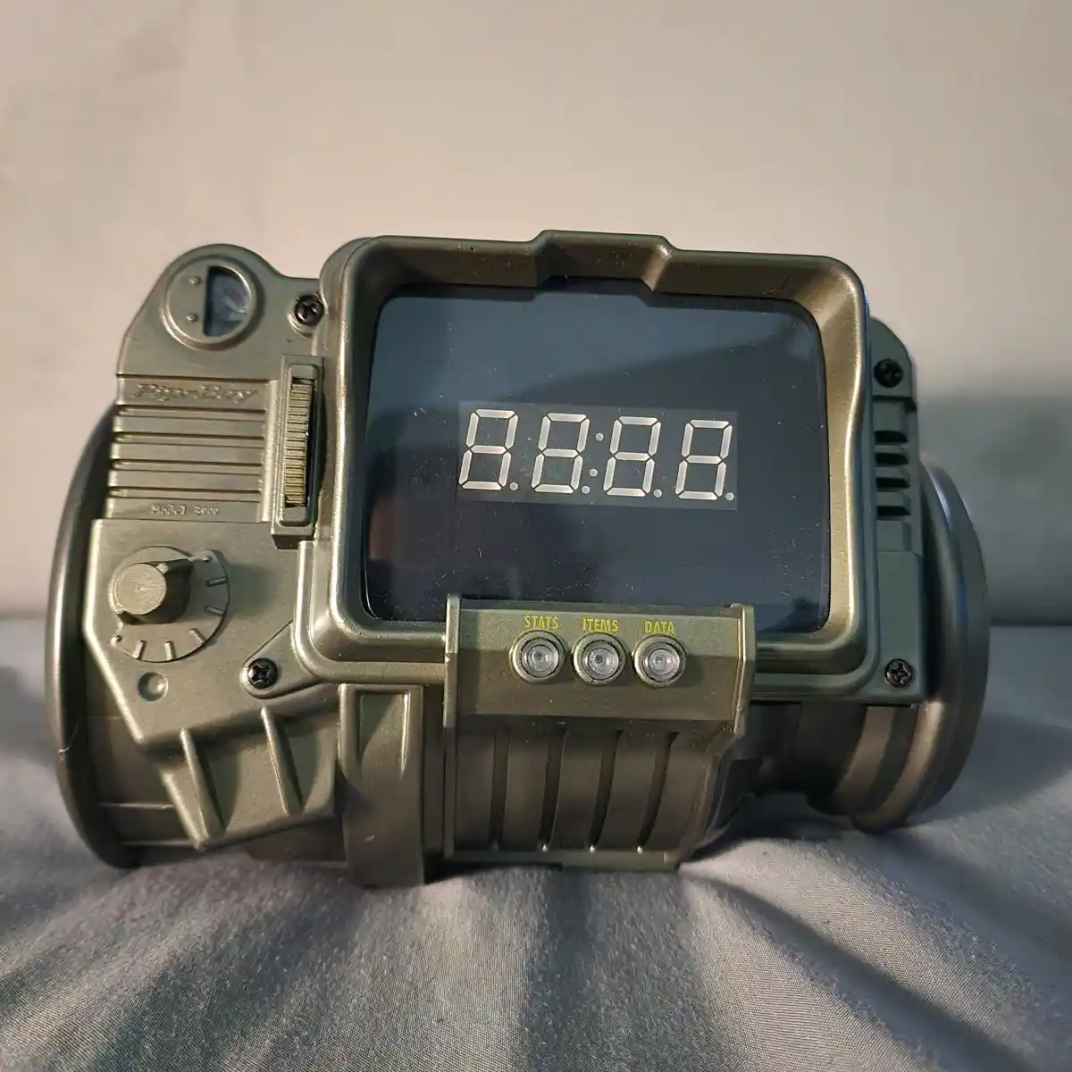 A close-up of a green, rugged Pip-Boy 3000 device, resembling a Fallout game gadget, with its digital screen displaying…