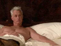 A six-panel image sequence shows a shirtless man with white hair lying in bed, covered by white sheets, looking directly at…