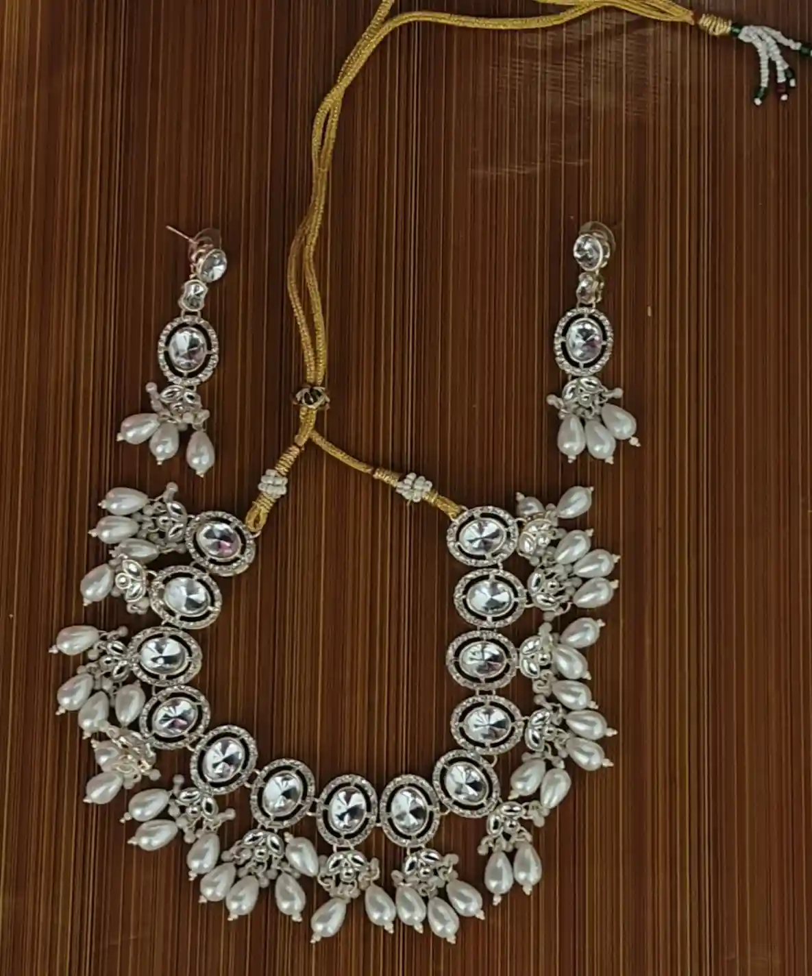 An ornate silver and gold jewelry set with large central stones, dangling pearl-like beads, and matching earrings, displayed…