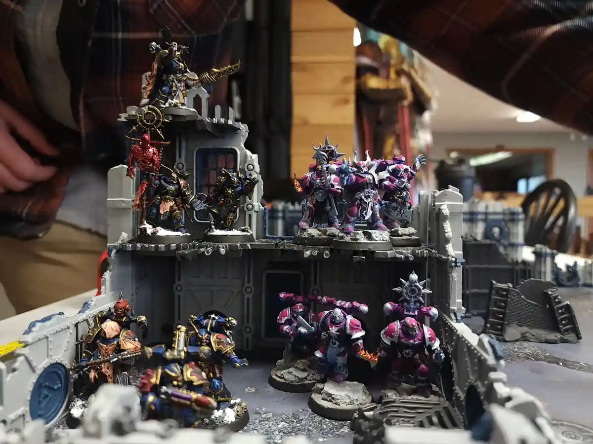 A photo of a detailed miniature wargaming scene with two opposing armies of painted figurines on a multi-level terrain…