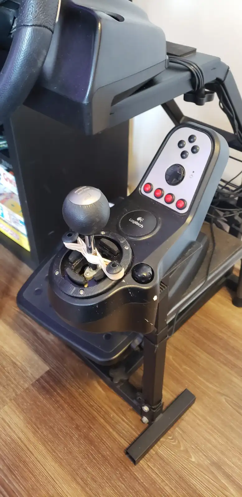 A Logitech racing wheel and pedal set is shown with its gear shifter mechanism visibly broken, with white plastic pieces…