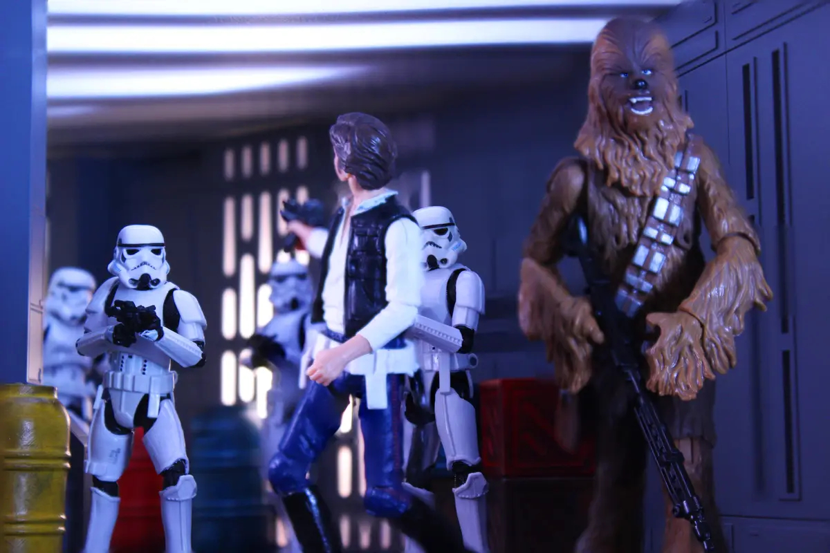 A photo of Star Wars action figures shows Han Solo facing Stormtroopers while Chewbacca stands beside him with a wide…