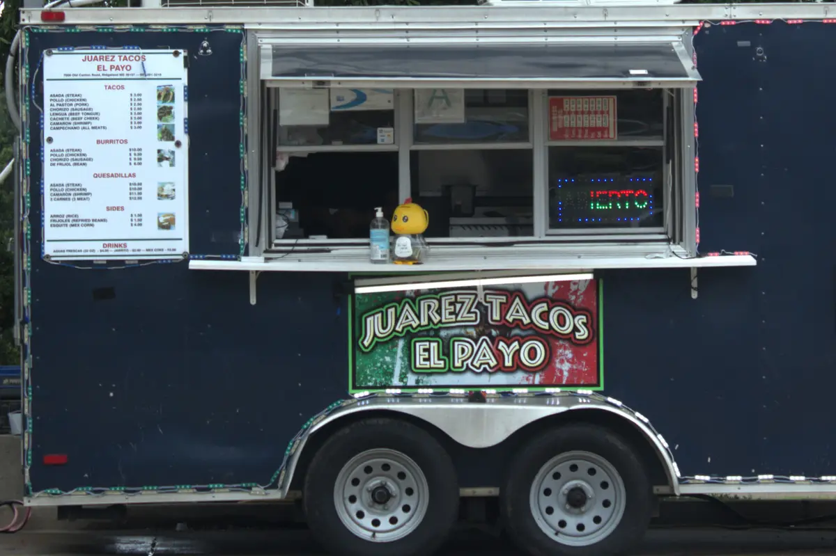 A dark blue food truck named 'Juarez Tacos El Payo' has a menu listing tacos, burritos, and drinks with prices. At the…