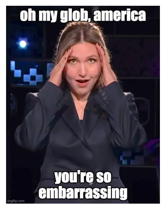 A woman in a dark blazer holds her hands to her temples with a face of exasperated disbelief, set against a dimly lit stage…