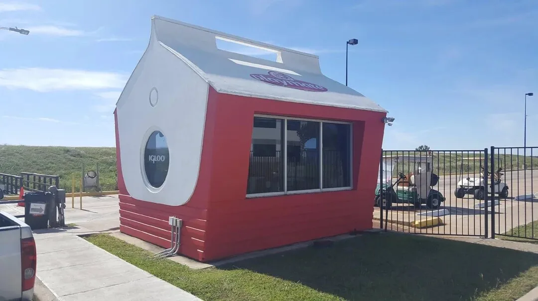 A red and white building shaped like a giant milk carton with the word 'iqlloo' written in a circular window. The roof has a…