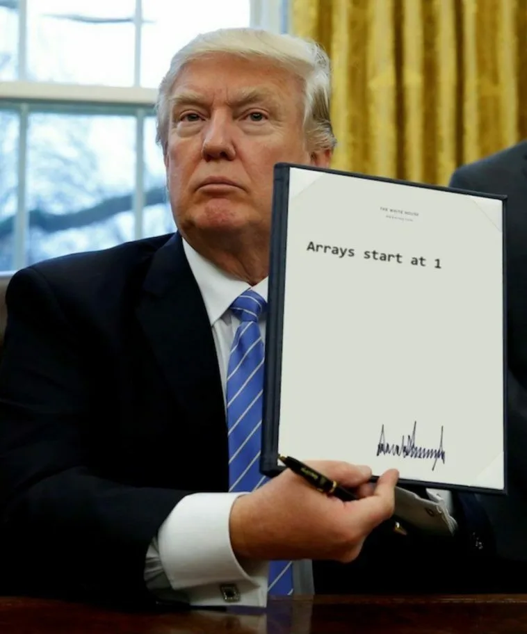 A man in a dark suit and blue striped tie sits at a desk holding a framed document that reads 'Arrays start at 1' with a…