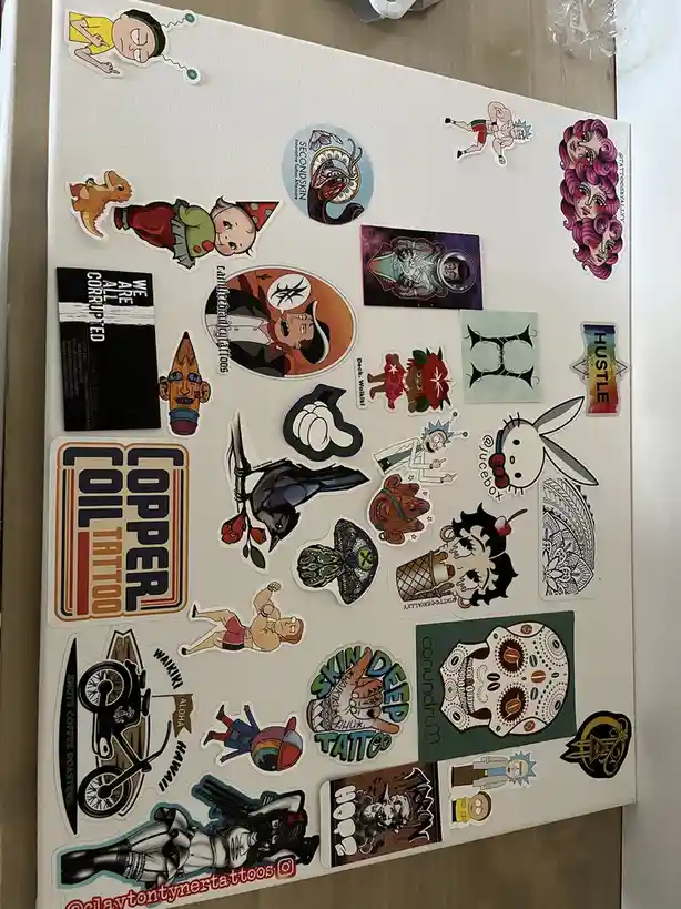 A white canvas or board is covered with numerous colorful stickers featuring cartoon characters like Rick and Morty…