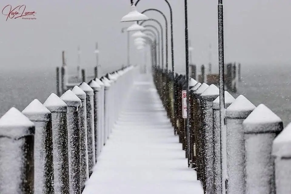 A snowy pier with snow-covered railings and lampposts receding into the foggy distance. Overlaid text reads 'i'm not crying…