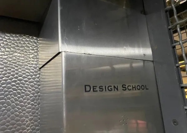 A close-up photo of a stainless steel wall panel with the words 'DESIGN SCHOOL' engraved on it. The panel is part of a…