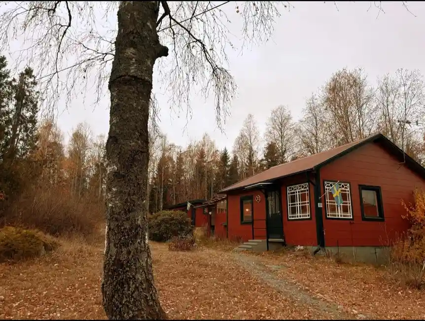A photo of a red wooden cabin in a forest with autumn leaves on the ground and bare trees, overlaid with the text 'i'm not…