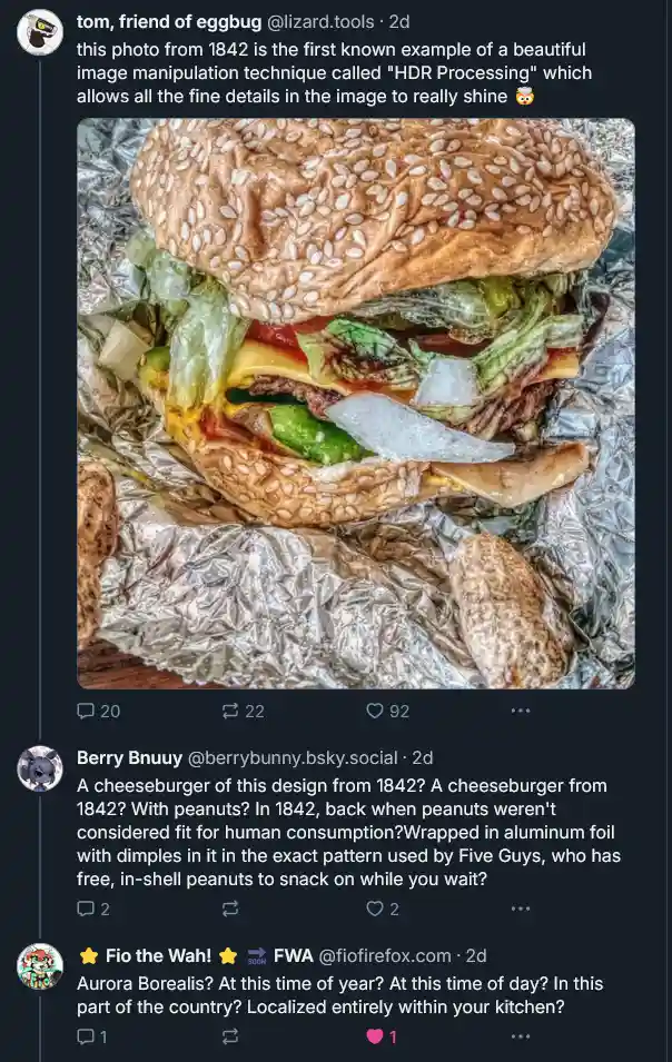 A close-up photo of a cheeseburger with sesame seed bun, lettuce, tomato, cheese, and onion, wrapped in crinkled aluminum…