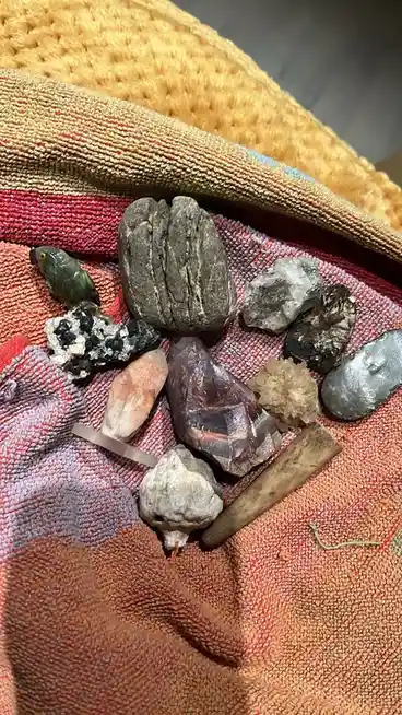 A collection of various rough and polished stones, crystals, and mineral specimens arranged on a colorful, textured woven…