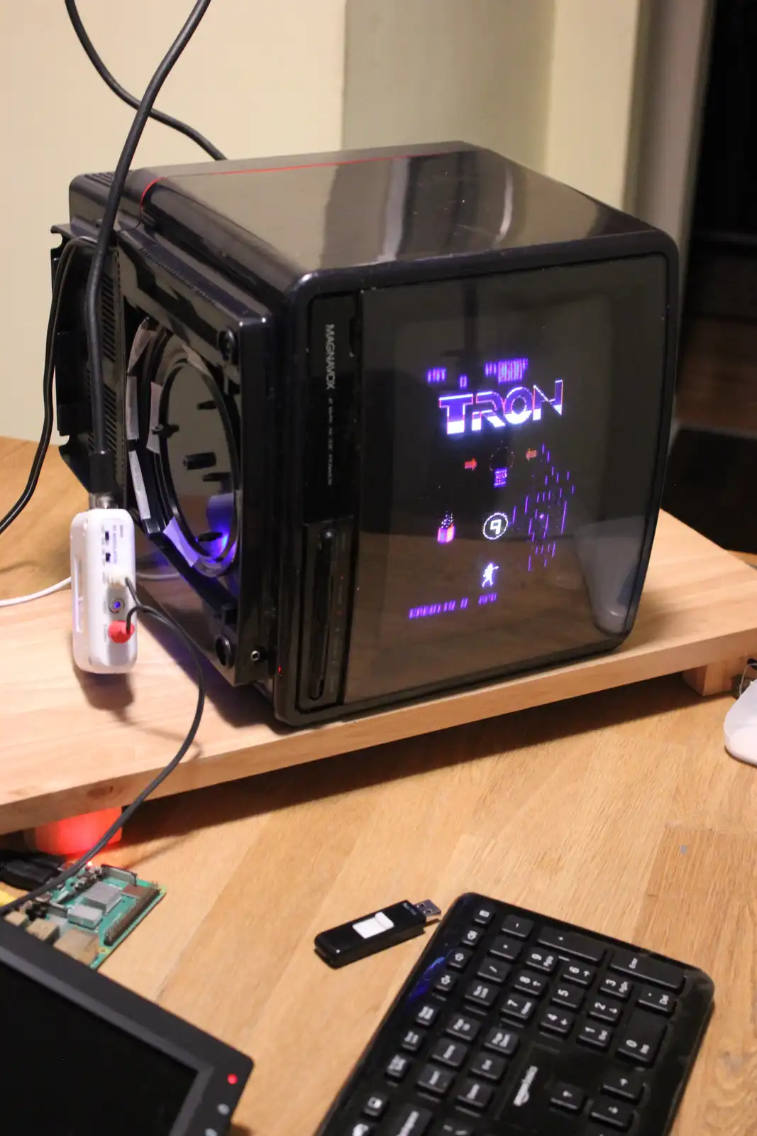 A black computer case with a transparent side panel displays the classic TRON video game on its screen, featuring glowing…