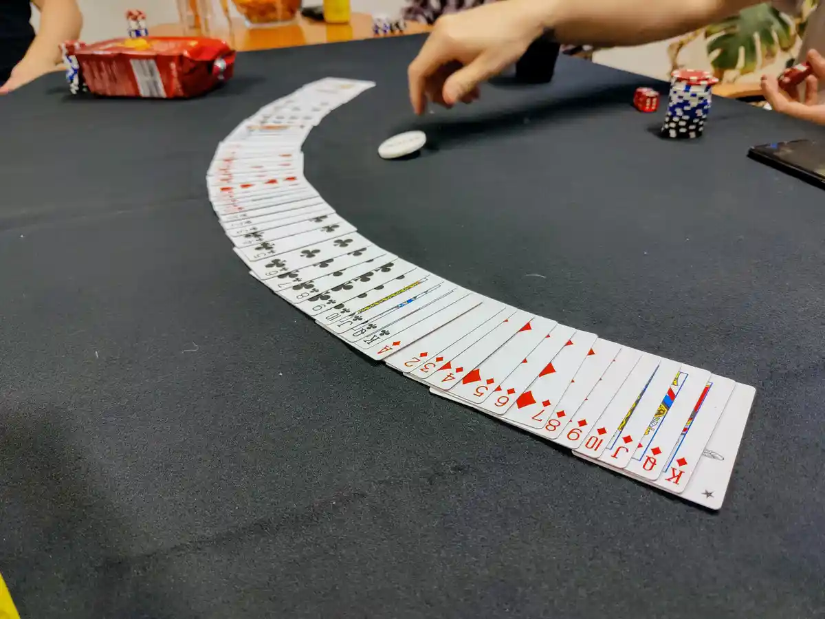 A curved arc of playing cards laid out on a black felt table, showing all 52 cards in sequence from ace to king across…
