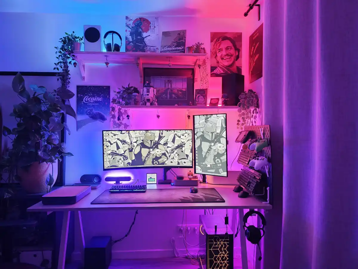 A highly customized gaming or streaming desk setup bathed in vibrant purple and blue LED lighting, featuring two monitors…