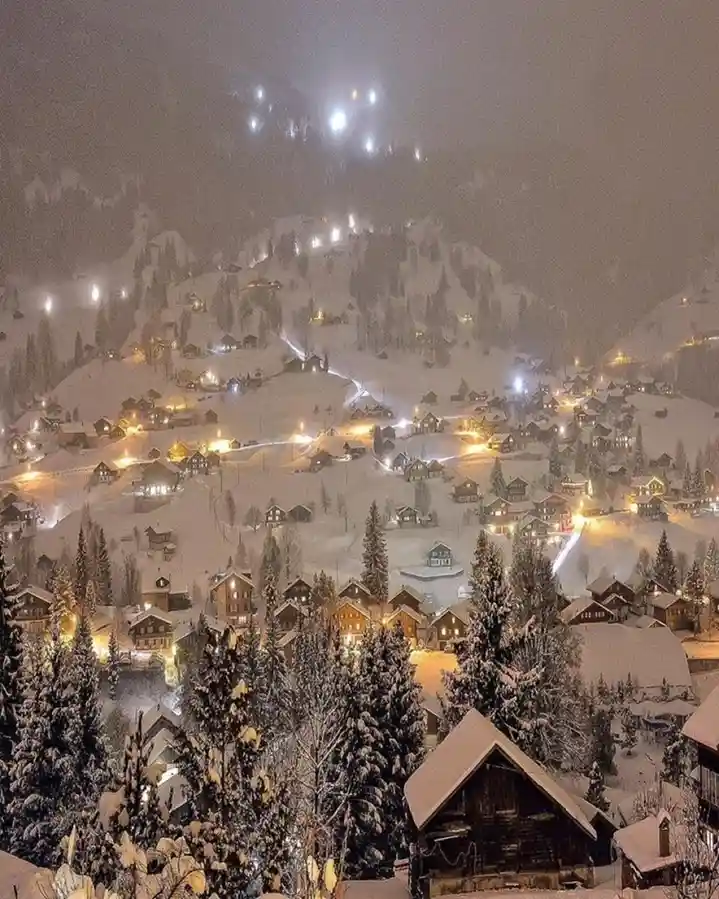 A snowy mountain village at night, with illuminated chalets and ski resort lights on the slopes. Overlaid text reads 'i'm…