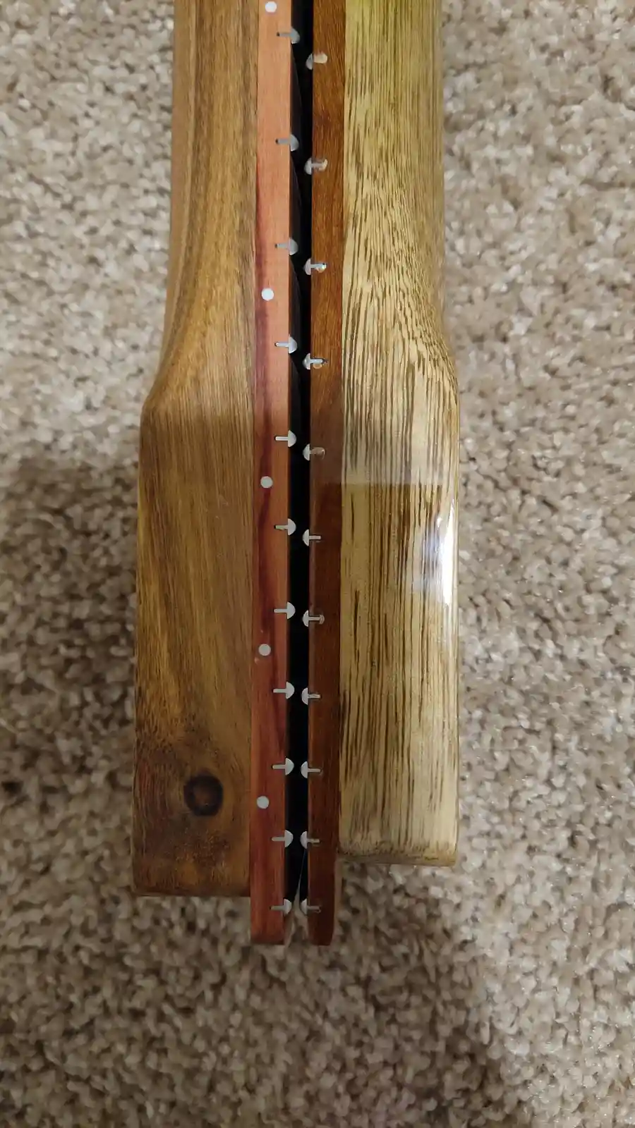 A close-up photo shows the back of a wooden guitar neck, revealing its internal construction with metal pins and a dark wood…