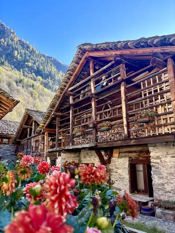 a picturesque mountain village scene featuring traditional wooden houses with stone foundations and slate roofs, adorned…