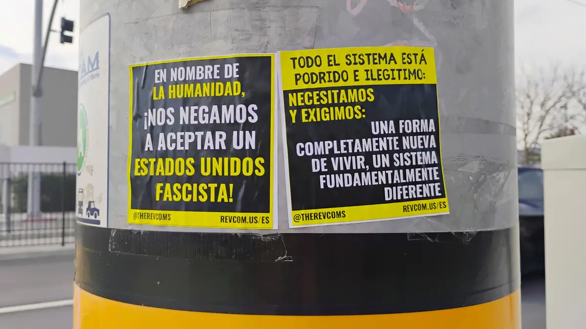 Two black-and-yellow protest posters are taped to a gray utility pole with black and yellow stripes. The left poster…