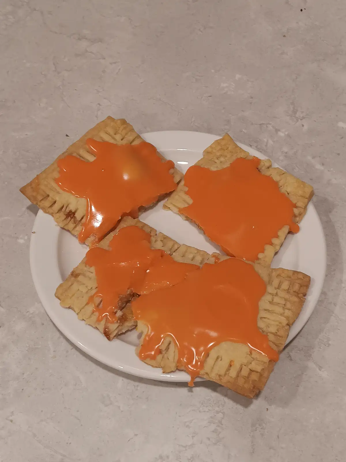 Four golden-brown, square-shaped pop-tarts are arranged on a white plate, each generously covered with a thick, glossy…