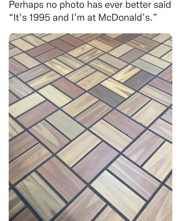 A close-up photo of a floor made of rectangular tiles arranged in a herringbone pattern, each tile mimicking the look of…