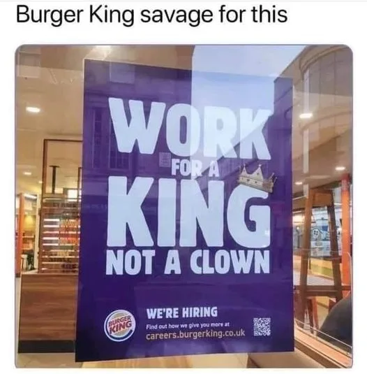 A purple Burger King recruitment poster visible through a glass storefront window reads 'WORK FOR A KING NOT A CLOWN' with a…
