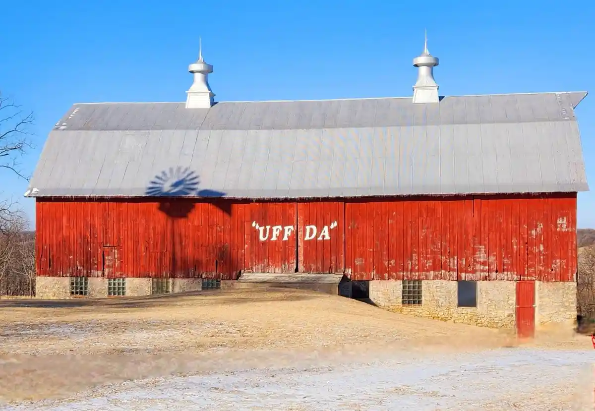 A large red barn with a gray metal roof and two white cupolas stands under a clear blue sky. The barn's red wooden siding…