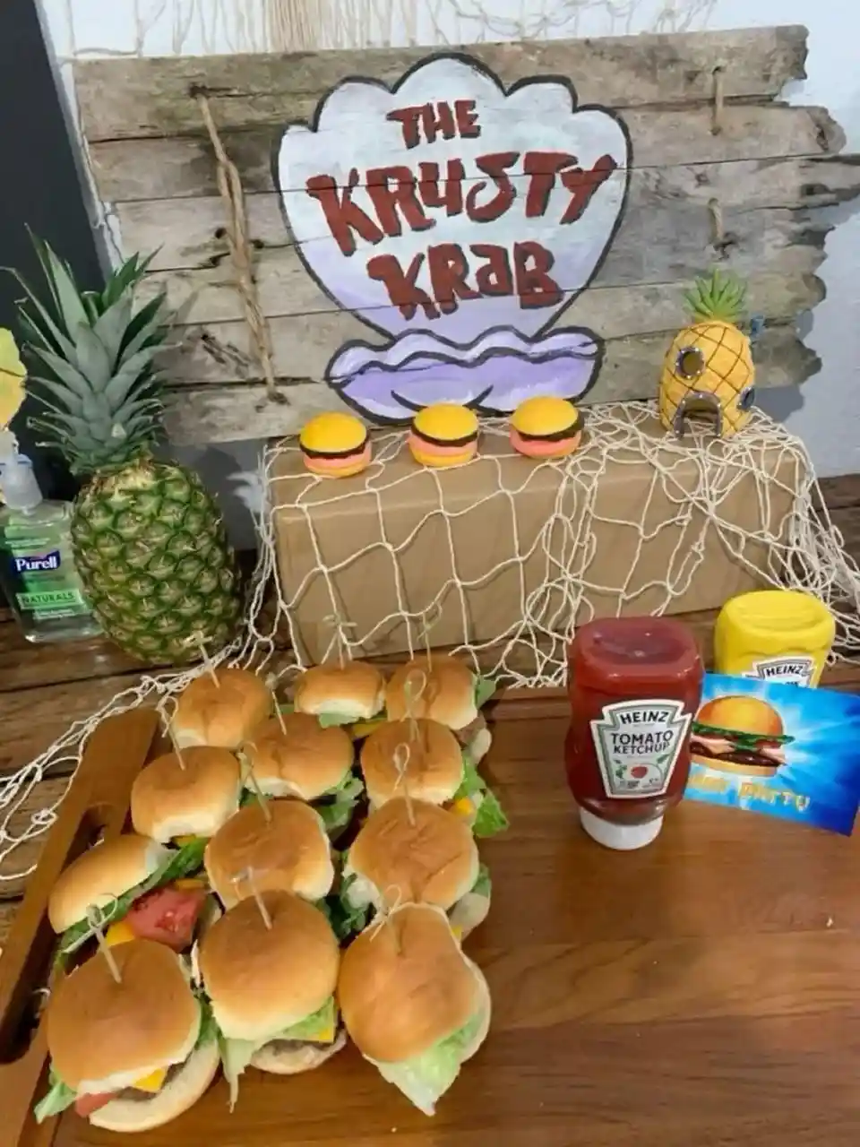 A homemade SpongeBob SquarePants themed party setup features a wooden sign reading 'THE KRUSTY KRAB' above a table covered…