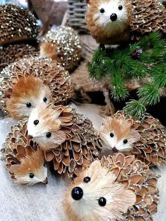 A close-up photo shows several pinecones decorated to resemble hedgehogs, with small black bead eyes, fluffy white and brown…