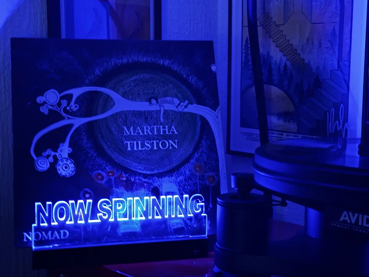 A blue-lit vinyl record display shows the album cover for Martha Tilston's 'Nomad', featuring an illustration of a person…