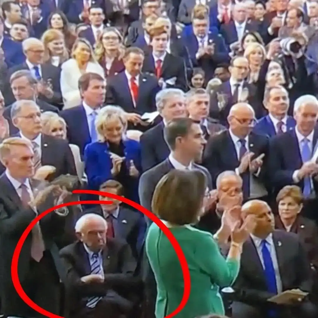 a crowded political event with many people in suits clapping enthusiastically, while an older man with white hair and a…