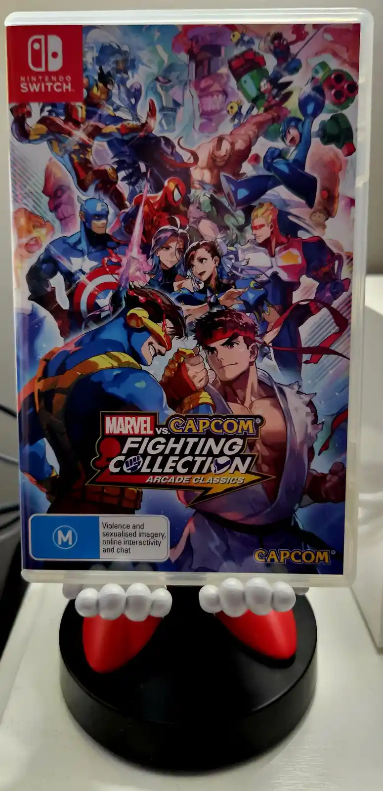A Nintendo Switch game case for 'Marvel vs. Capcom Fighting Collection: Arcade Classics' is displayed on a stand shaped like…