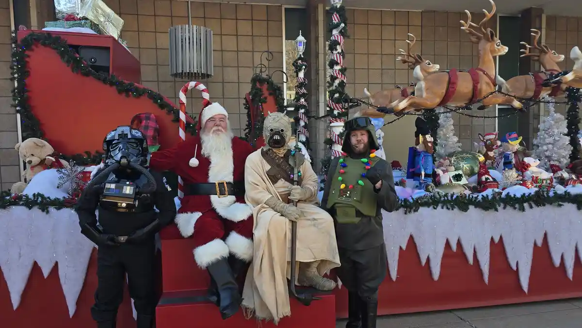 Four people dressed as Santa Claus, a stormtrooper, a jedi, and a rebel soldier are posing together in front of a festive…