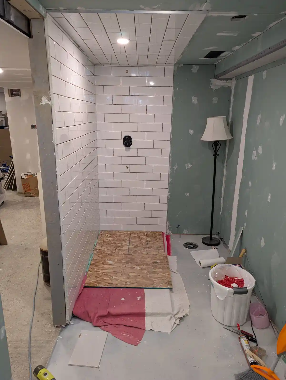 A bathroom under renovation shows one wall fully tiled in white subway tiles with a shower fixture, while the adjacent walls…