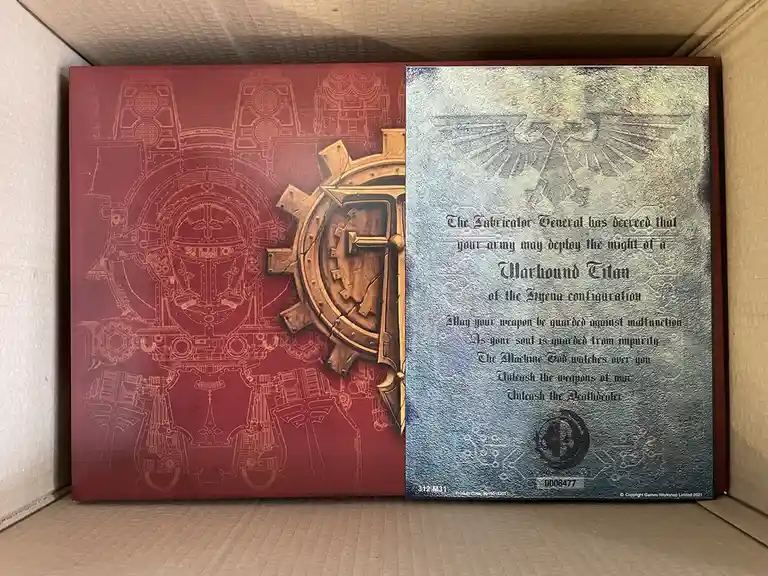 A Warhammer 40,000 Warhound Titan box insert with a red side showing mechanical schematics and a silver side with embossed…