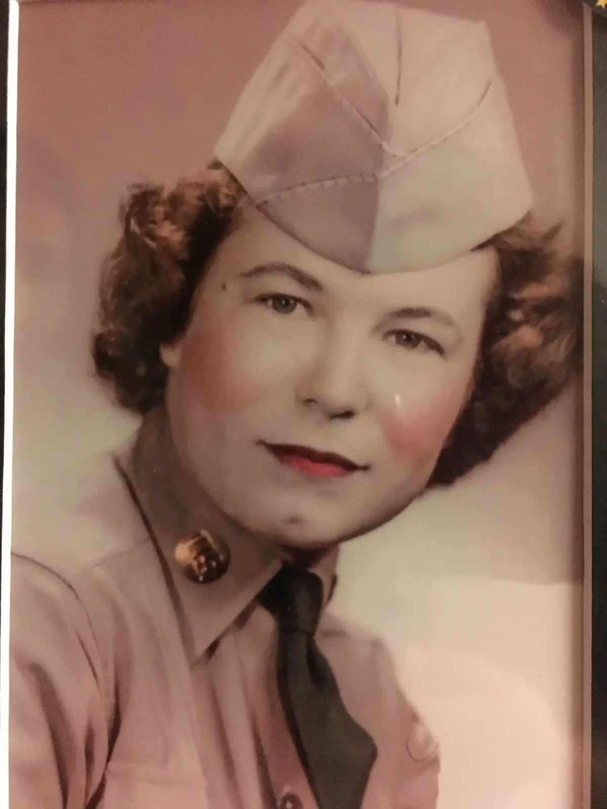 A vintage, sepia-toned portrait of a woman in a military-style uniform and cap, with a tear visible on her cheek. The…