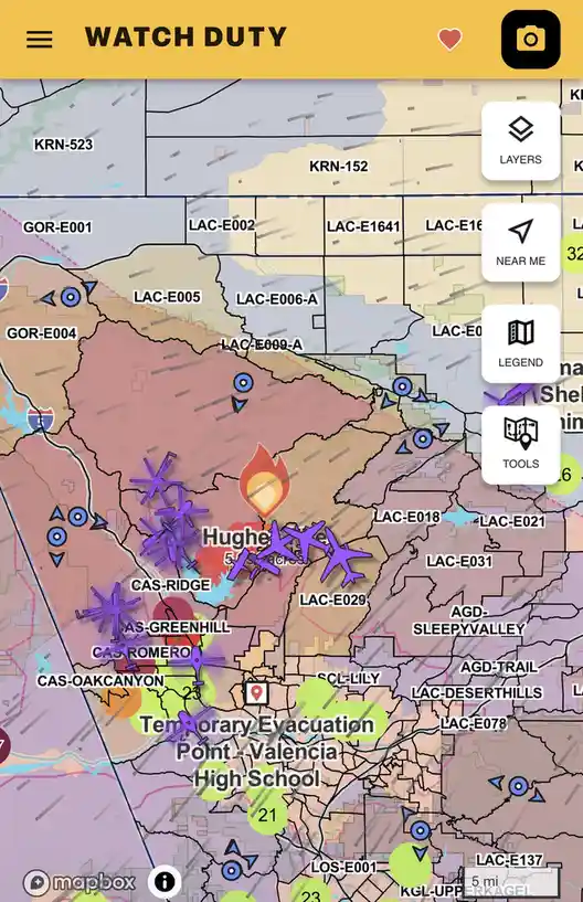 A screenshot of a 'WATCH DUTY' app map showing a wildfire in the area of Hughes, with numerous purple airplane icons…
