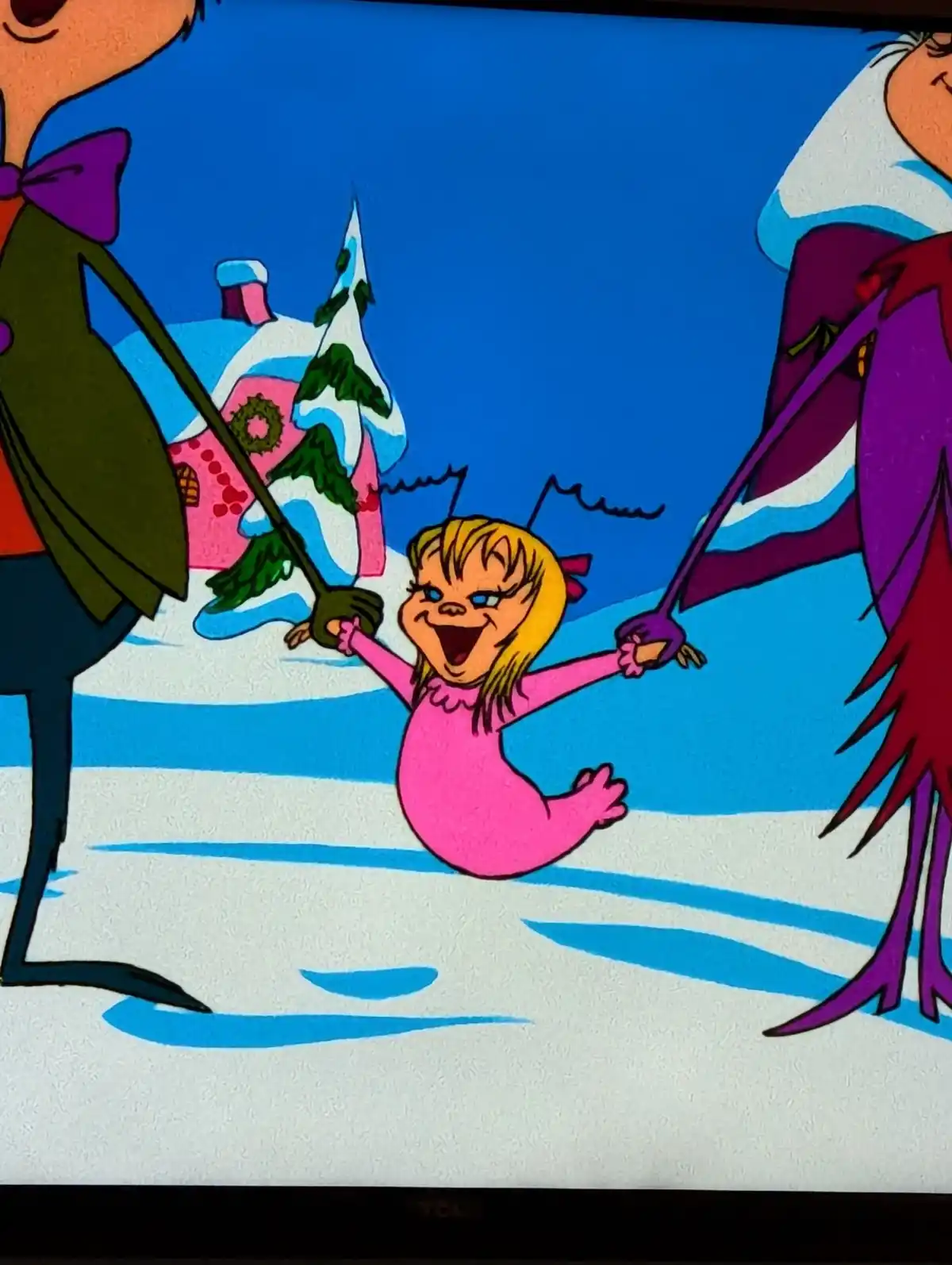 A cartoon image shows a joyful, blonde-haired child in a pink outfit being swung between two adults in a snowy landscape…