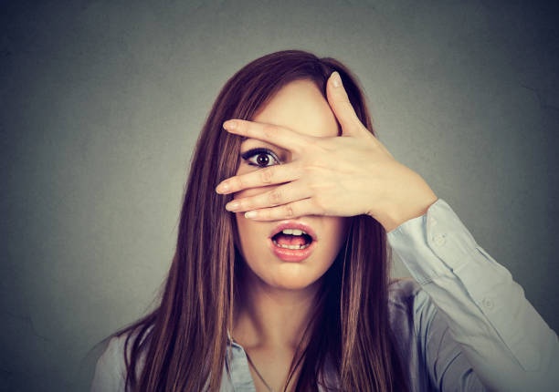 a woman with long brown hair and a light blue shirt covers her eyes with her hand, leaving only one eye visible, while her…