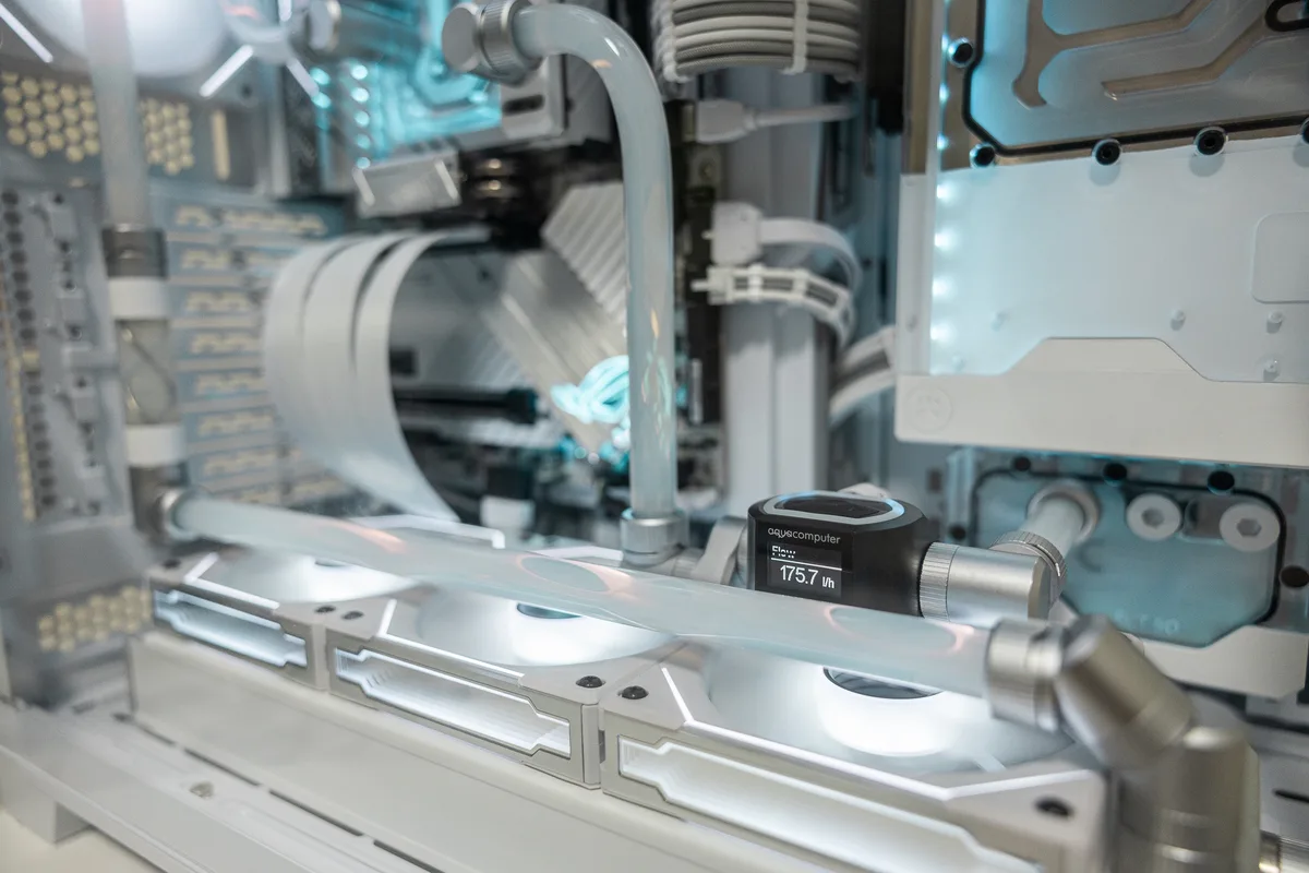 A close-up photo of a white liquid-cooled computer case with transparent tubing and glowing blue LED lights. A small black…